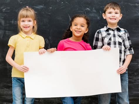 Tres niños lindos sosteniendo una hoja de papel vacía para el anuncio