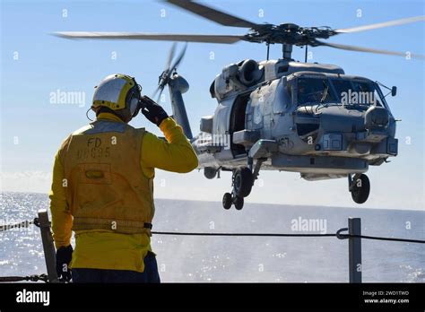 Boatswain S Mate Signals To An MH 60R Sea Hawk Helicopter During A