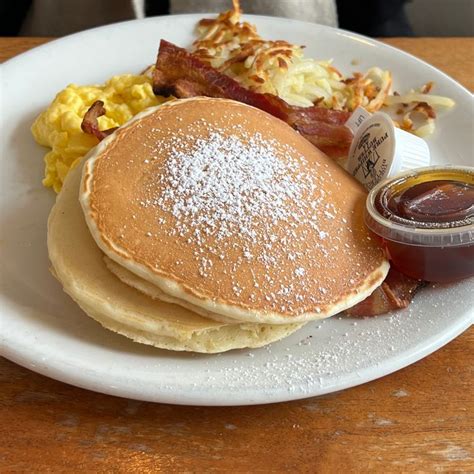 Pancakes With Bacon Eggs And Syrup On A White Plate Next To Some