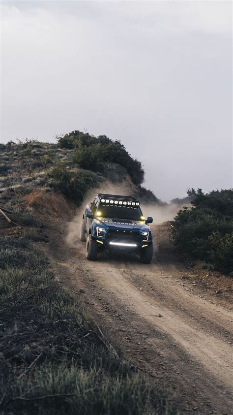 A Truck Driving Down A Dirt Road With Trees On The Side And Fog In The Air