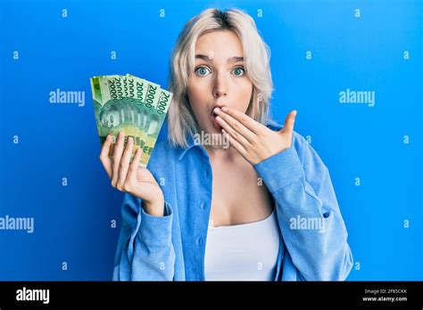 Jeune fille blonde portant des billets de roupie indonésiens couvrant la bouche avec la main
