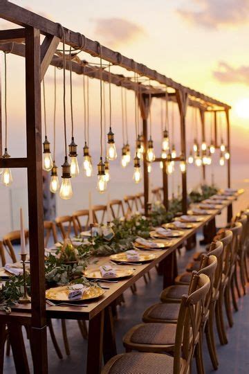 A Long Table Set Up With Hanging Lights And Place Settings For Dinner