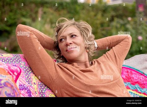 Smiling Woman Sitting With Hands Behind Head On Sofa At Back Yard Stock