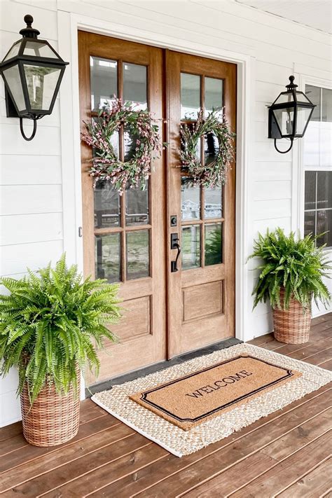 Two Potted Plants Sitting On The Front Porch Next To A Door With Wreaths