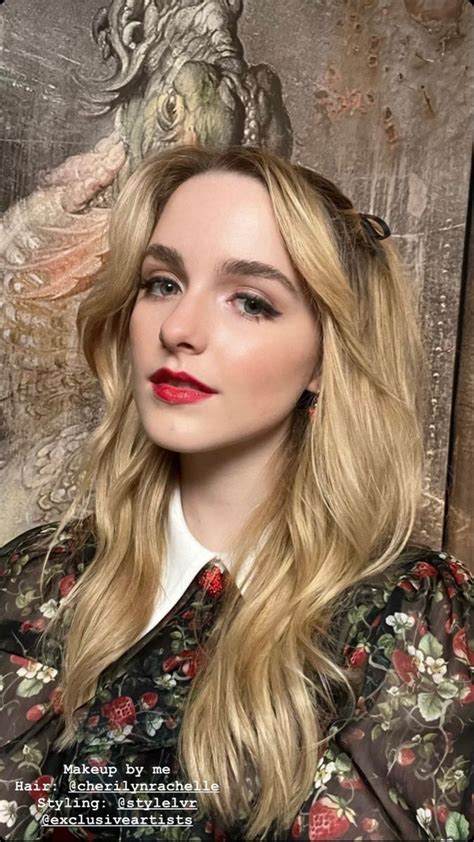 A Woman With Long Blonde Hair Wearing A Floral Shirt And Red Lipstick