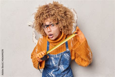 Horizontal Shot Of Curly Haired Female Builder Holds Measuring Tape