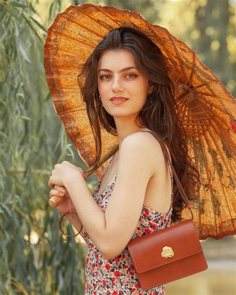 A Woman In A Dress Holding An Orange Parasol And Carrying A Brown Purse