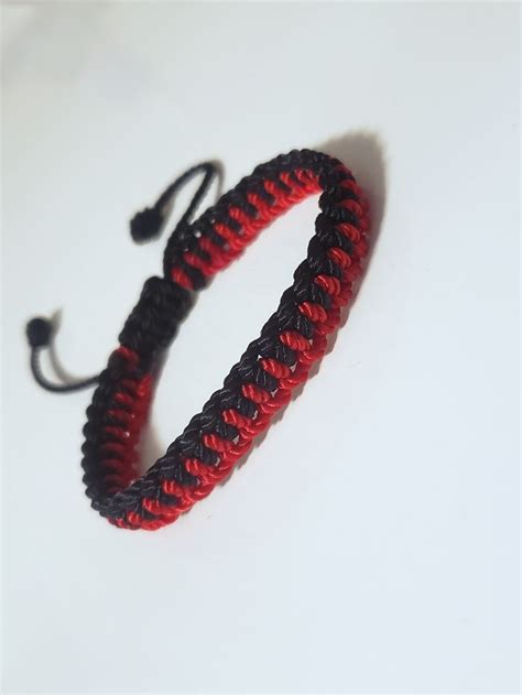 A Red And Black Braided Bracelet Sitting On Top Of A White Table