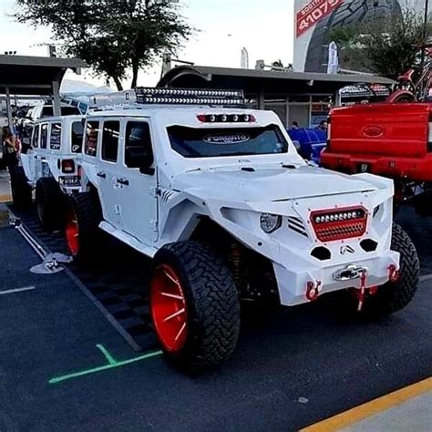 A White Jeep With Red Rims Parked In A Parking Lot Next To Other Vehicles