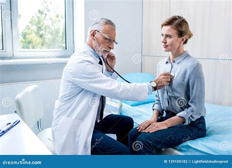 Serious Mature Male Doctor Examining Female Patient By Stethoscope