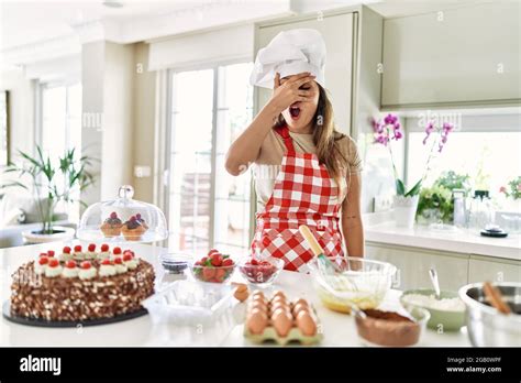 Beautiful Young Brunette Pastry Chef Woman Cooking Pastries At The Kitchen Peeking In Shock