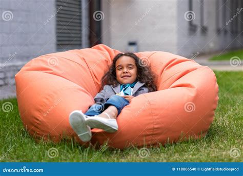 Cute Little African American Girl Lying On Bean Bag Chair And Looking