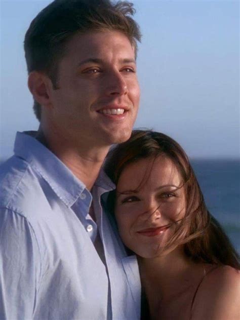 A Man And Woman Standing Next To Each Other Near The Ocean