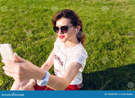 Close Up Of A Girl Sitting On The Green Grass In The City Park Girl Wears A White T Shirt Red