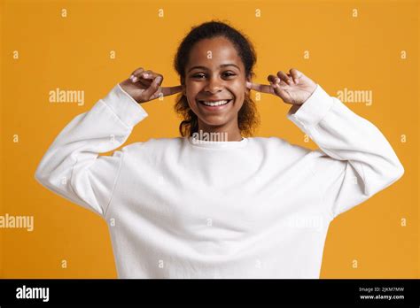 Brunette Black Girl Laughing While Plugging Her Ears Isolated Over Yellow Background Stock Photo