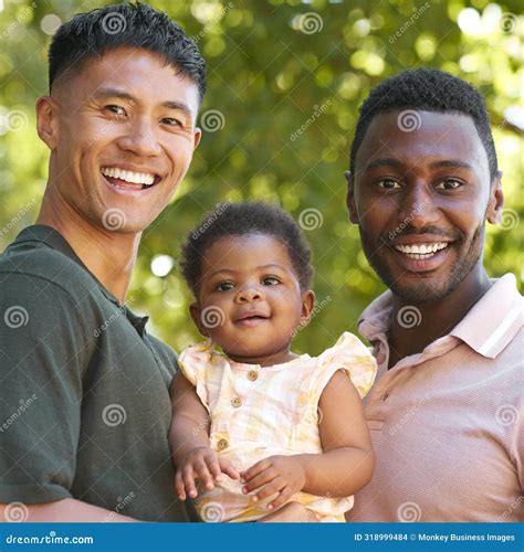 Portrait Of Same Sex Male Couple Or Friends Cuddling Baby Outdoors In Garden Or Countryside