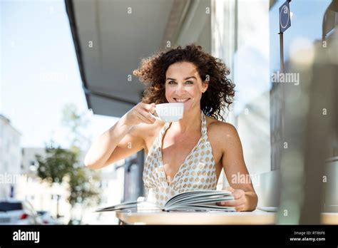 Mature Woman Sitzting In Cafe Reading Book Drinking Coffee Stock