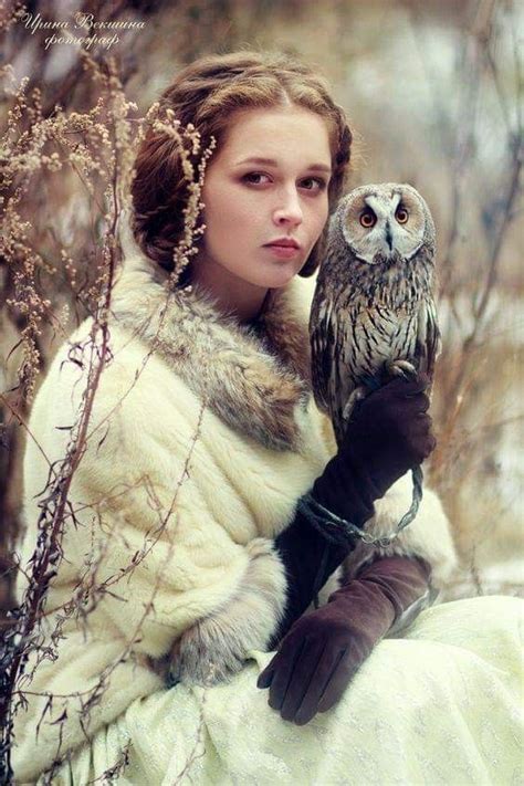 A Woman In A Fur Coat Holding An Owl On Her Arm While Sitting Next To A