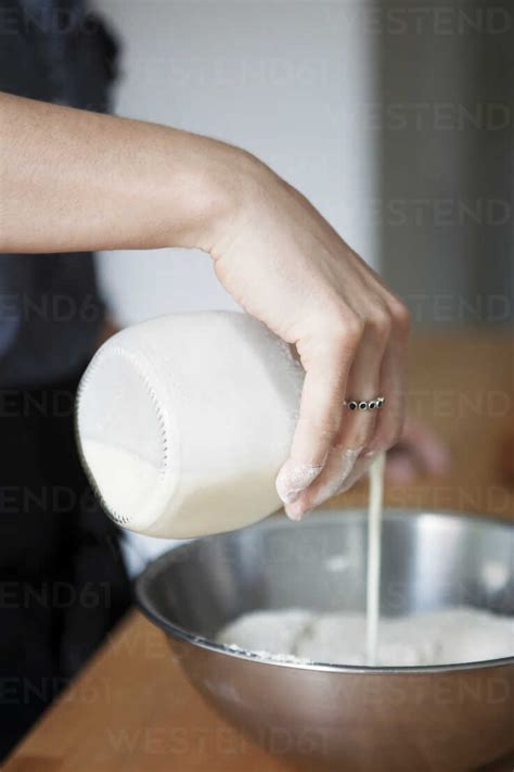 Cropped Image Of Hand Pouring Milk On Flour In Bowl Stock Photo