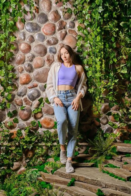 Linda Mujer Apoyada En El Antiguo Muro De Piedra Cubierto De Plantas