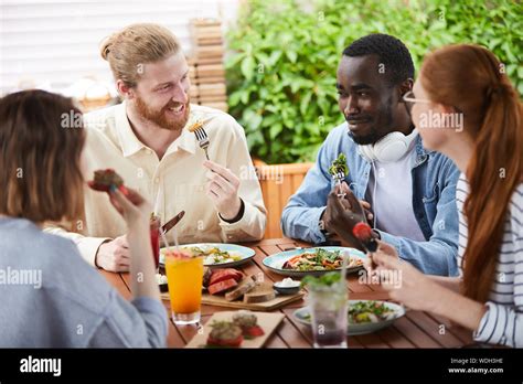 Group Of Friends Talking And Smiling To Each Other While Eating Meal At