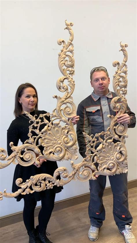 Two People Standing Next To Each Other Holding Large Wooden Sculptures