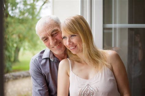Recht Schöne Blonde Stellung Nahe Dem Fenster Mit Ihrem älteren Ehemann Und Lächeln Alters