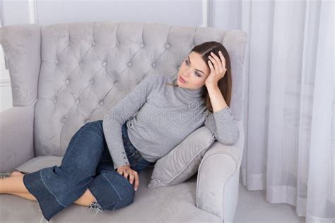 A Beautiful Brunette Sits On A Grey Sofa Stock Photo Image Of Friendly Jeans