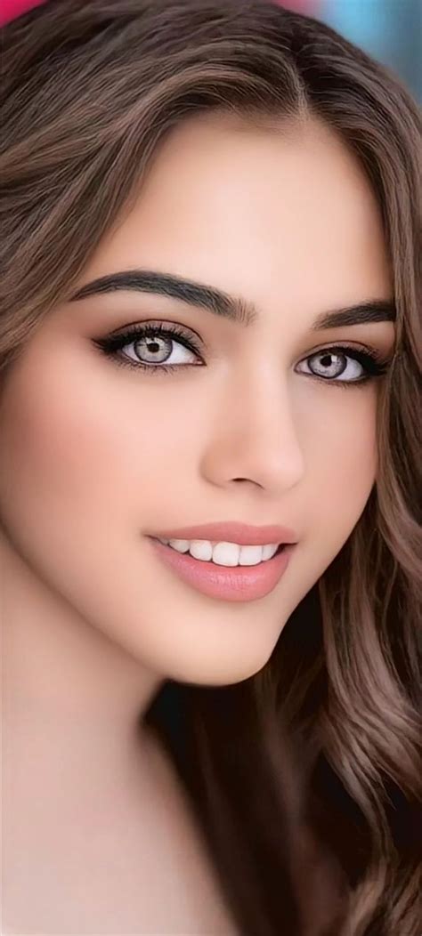 A Woman With Long Brown Hair And Blue Eyes Posing For A Photo In Front Of A Pink Background