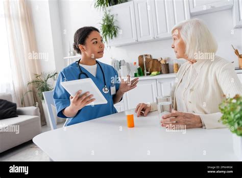Brunette Multiracial Nurse Using Digital Tablet And Holding Medication