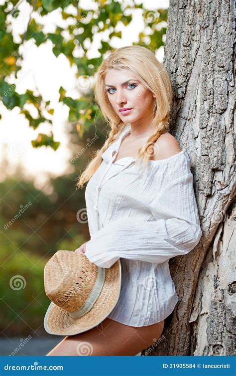 Femme Blonde Très Mignonne S asseyant Extérieur Avec Un Chapeau Près D un Arbre Images stock