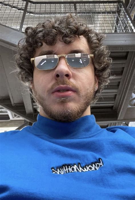 A Man With Curly Hair Wearing Sunglasses In Front Of A Metal Caged Area