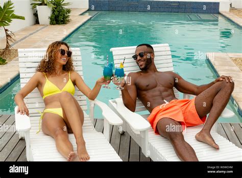 Couple Toasting Glasses Of Cocktail While Relaxing On A Sun Lounger