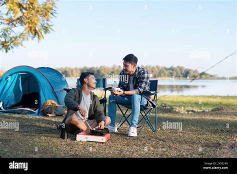 Couple Gay Lgbt Sitting In Camp Cooking And Near River In Mountains