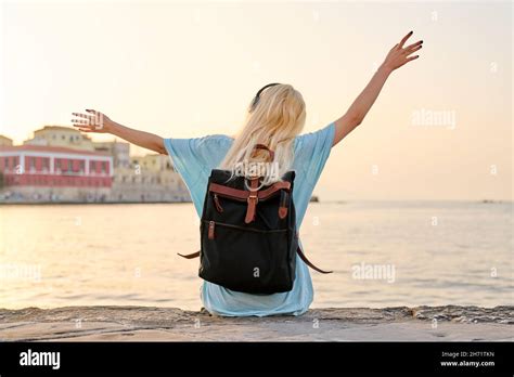 Back View Blonde Woman In Headphones With Backpack Sitting On City Sea