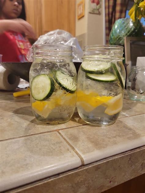 Two Mason Jars Filled With Cucumbers And Lemon Slices Sitting On A