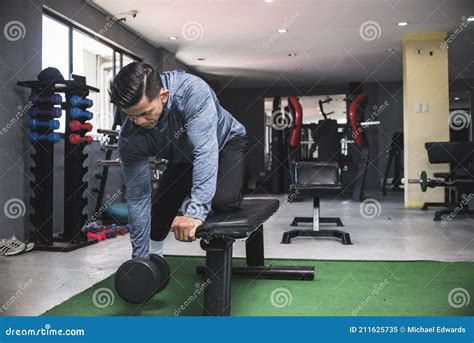 A Muscular and Buff Man in a Sweatshirt Does One Arm Dumbbell Rows ...