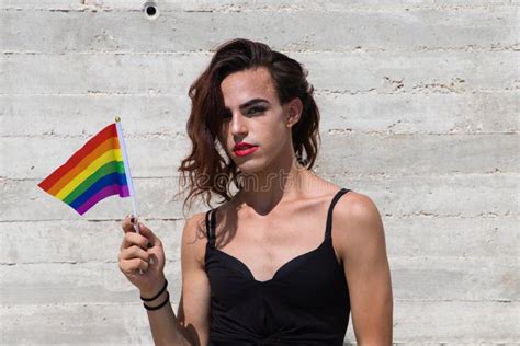 Young Latin And Transsexual Woman On Grey Background Holding The Gay Pride Flag With Her Hand