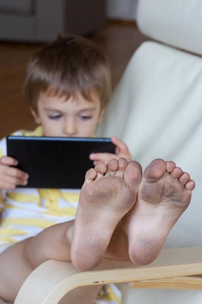 Pies sucios de un niño de cinco años sentado en el sillón con su