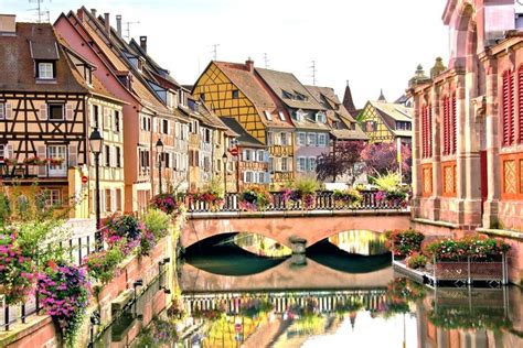 A River Running Through A City With Lots Of Buildings And Flowers