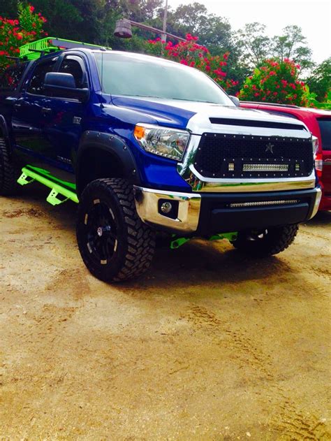 A Blue Truck Parked Next To Other Red And Green Trucks In A Parking Lot