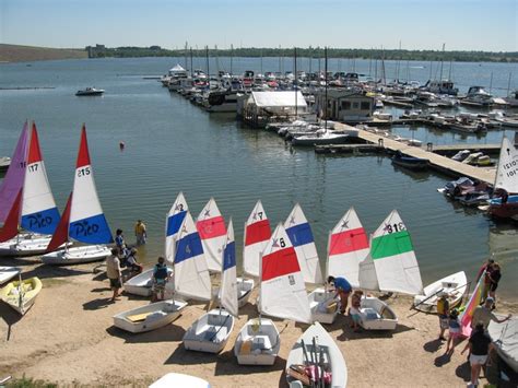 several sailboats are parked on the beach near boats in the water and people standing around them