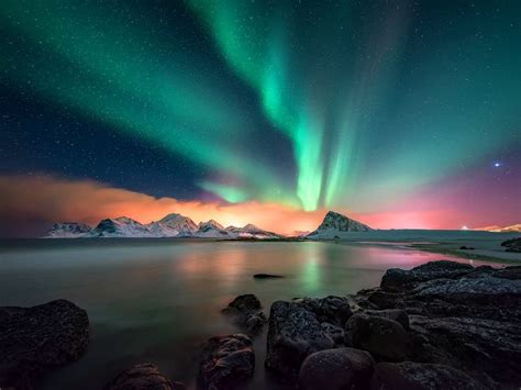 The Aurora Bore Is Shining Brightly In The Sky Over Water And Rocks