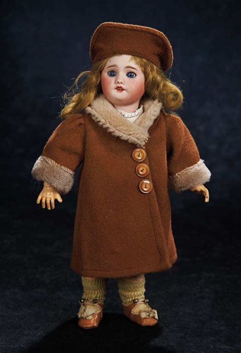 A Doll With Blonde Hair Wearing A Brown Coat And Hat Standing On A