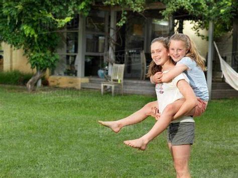 Teenage Girl Giving Her Sister Piggyback Ride In Garden Stock Photo