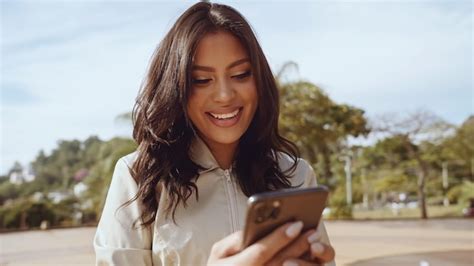 Linda jovem latina usando smartphone em pé na rua da cidade retrato de mulher latina sorridente