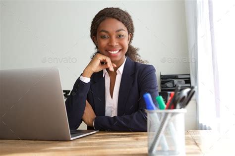 A Woman Sitting At A Desk In Front Of A Laptop Computer Smiling For The