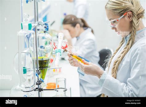 Young Female Scientist In Protective Glasses And Lab Coat Looking At Test Tubes In Laboratory