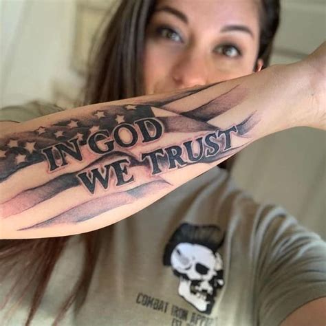 A Woman With A Tattoo On Her Arm That Says In God We Trust And An