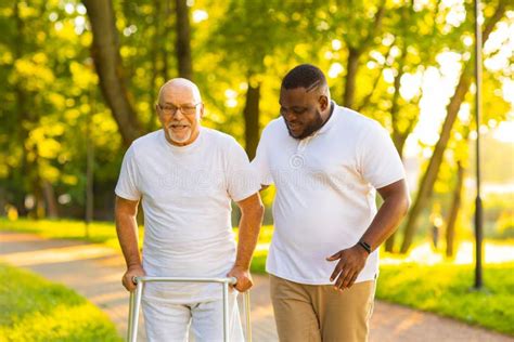 Caregiver Is Teaching Old Man To Walk With Walker Professional Nurse